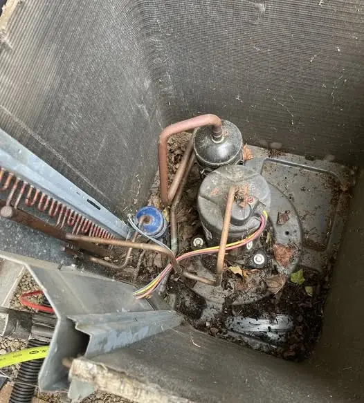 Leaves and debris inside an opened outdoor AC unit before maintenance