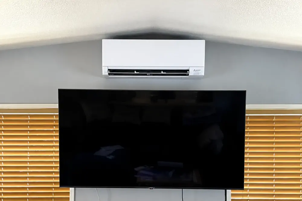 Mitsubishi indoor wall-mounted unit above a television between windows