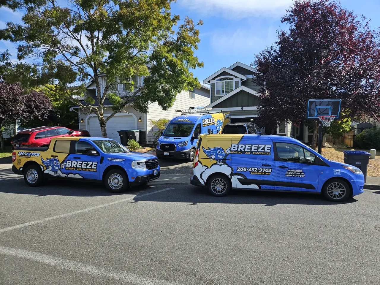 Three blue and yellow Breeze service vehicles parked on a residential street