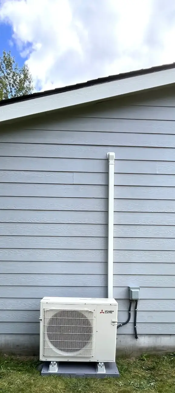 Mitsubishi outdoor heat-pump unit on a base beside gray house siding