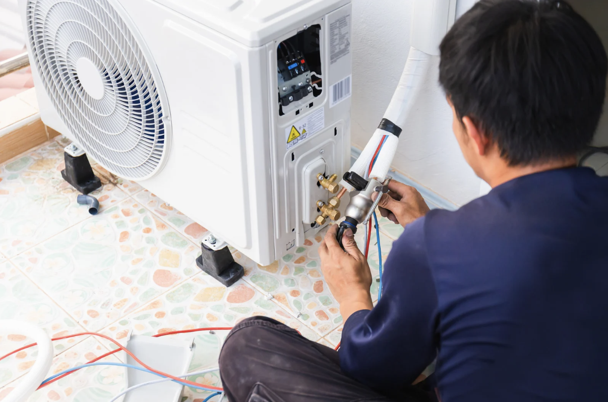 Technician performing maintenance on a ductless air conditioning unit, focusing on connections and refrigerant lines, relevant to late-summer AC tune-up services in Kent, WA.