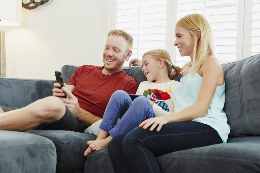 Family enjoying time together on a sofa, using a smartphone, reflecting warmth and comfort in a home setting.