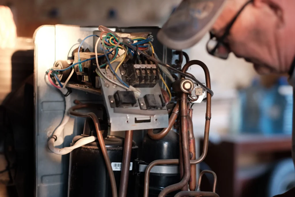 Air conditioner repair technician inspecting internal components, including wiring and copper tubing, in a residential HVAC unit.