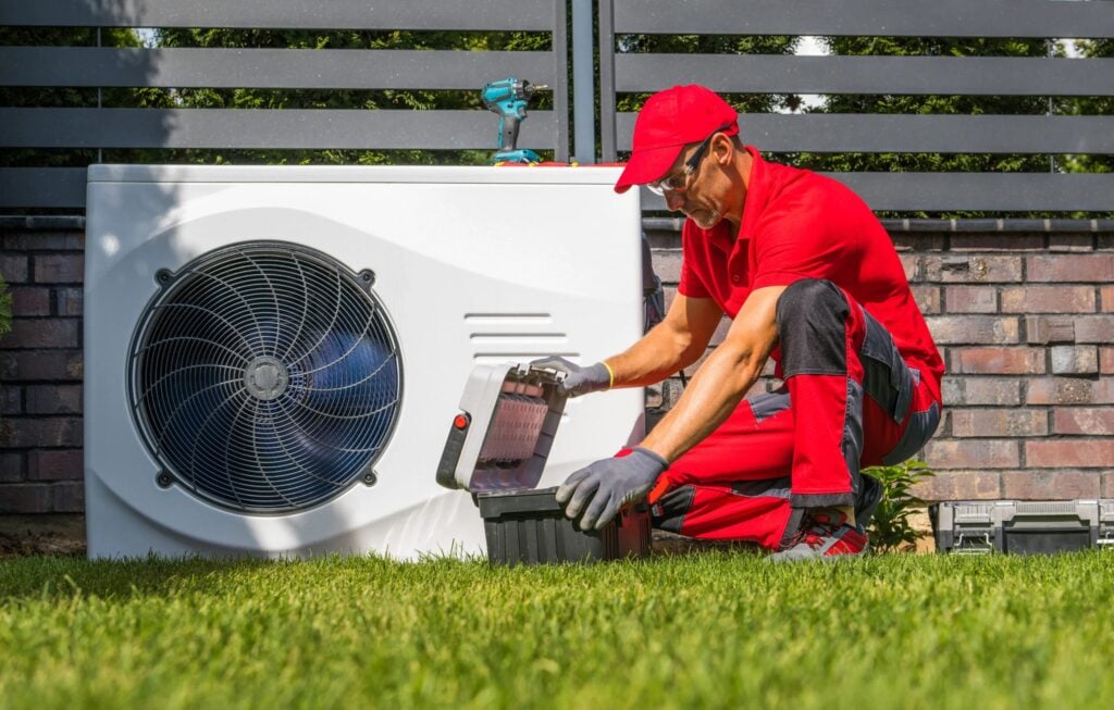 Technician in red uniform installing a heat pump outside a Kent home, emphasizing professional air conditioning services and energy efficiency.