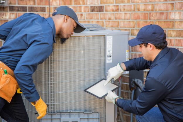 Two HVAC technicians inspecting and servicing an air conditioning unit outdoors, emphasizing professional maintenance and repair services in Covington, WA.