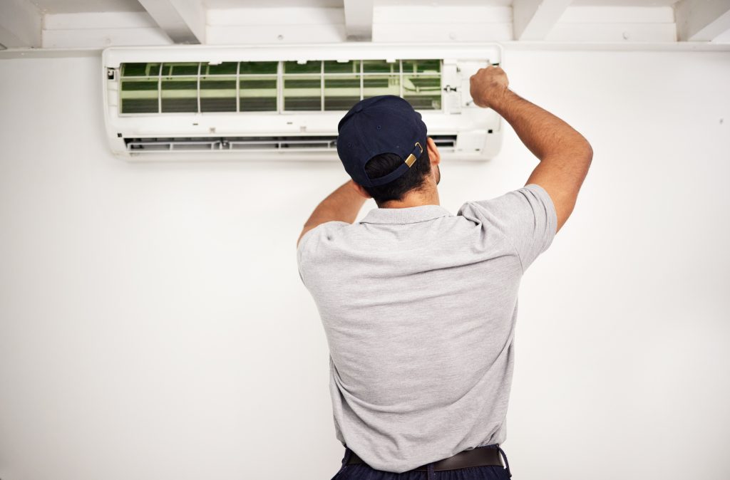HVAC technician installing a ductless mini split air conditioning unit on a white wall, showcasing professional installation services for energy-efficient home cooling.