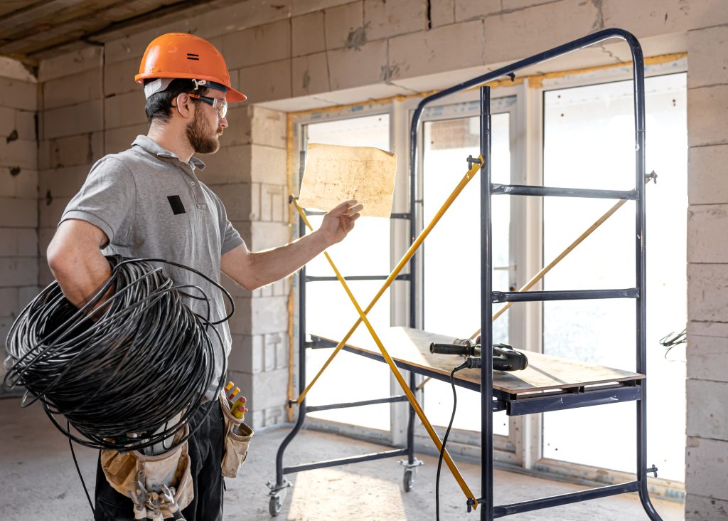 Electrician with wiring plans and cable for Whole Home Rewiring project. Planning electrical updates in Seattle, WA, inside new construction.