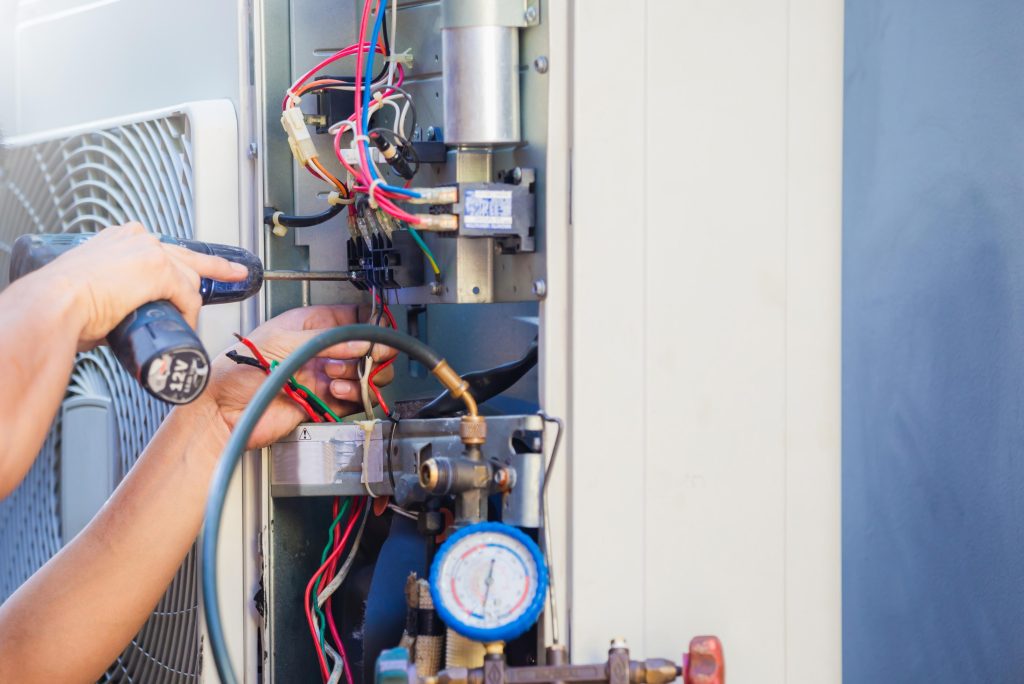 Air conditioning repair: Technician using a drill to fix an AC unit, highlighting the complexities of AC system maintenance in Seattle, WA.
