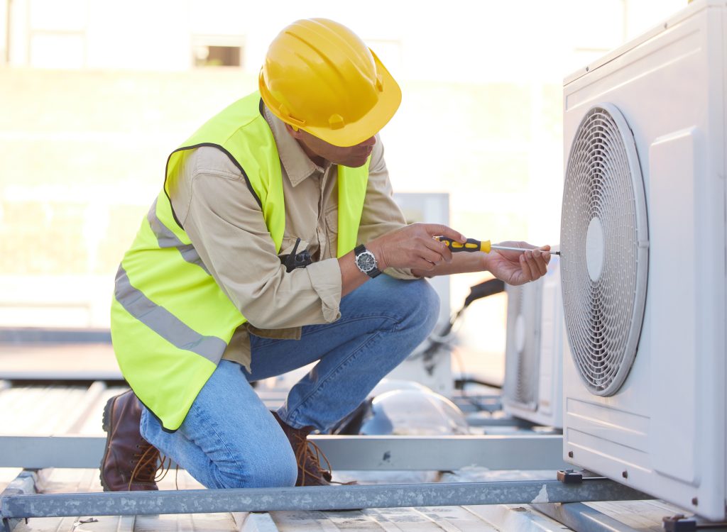Air conditioning technician wearing a hard hat and safety vest servicing an outdoor AC unit on a rooftop, emphasizing professional maintenance for optimal cooling performance in Kent homes.