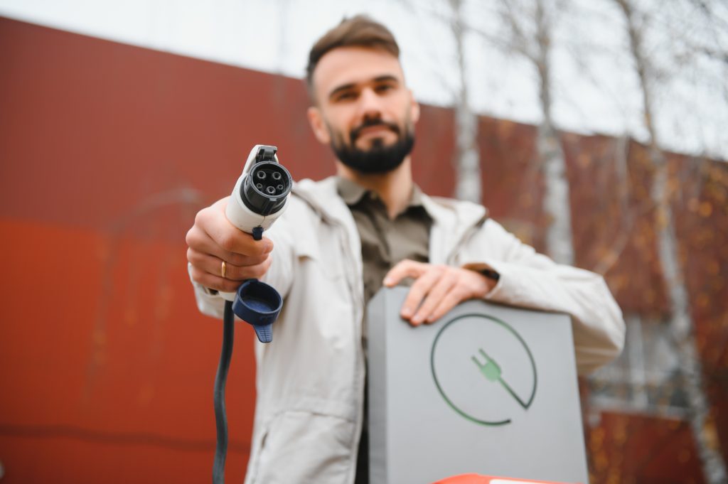 Man holding an electric vehicle charging plug, showcasing EV charging solutions for home installations by Breeze Heating Air & Electrical.