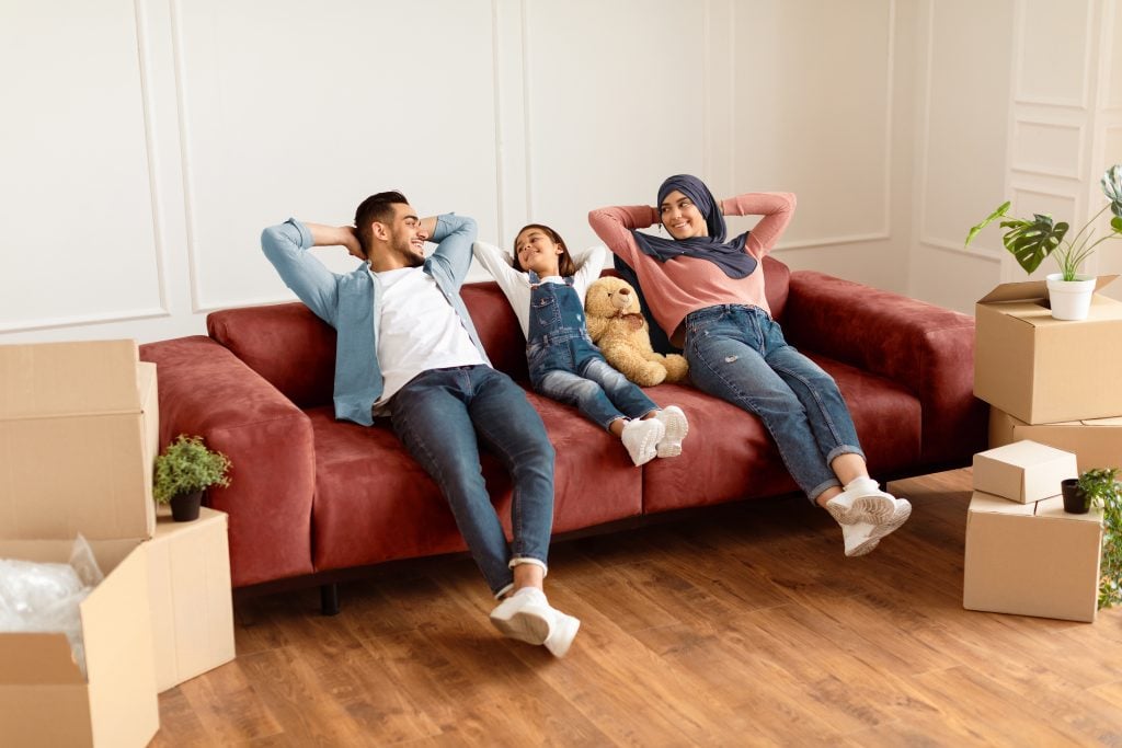 Relaxed family on sofa. Moving boxes suggest new home. Focus on home Heating Maintenance & inspection in Seattle, WA for comfort and safety.