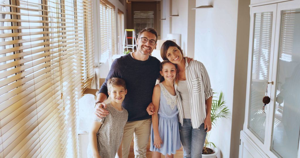Happy family smiling indoors near window blinds. Consider AC replacement for your home in Seattle, WA for optimal comfort.