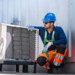 HVAC technician in Bellevue, WA, wearing a hard hat and safety vest, inspecting an outdoor AC unit. Find trusted HVAC contractors here.